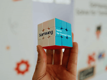 Holding a Rubik's Cube with the Samsung Solve for Tomorrow logo in one hand.
